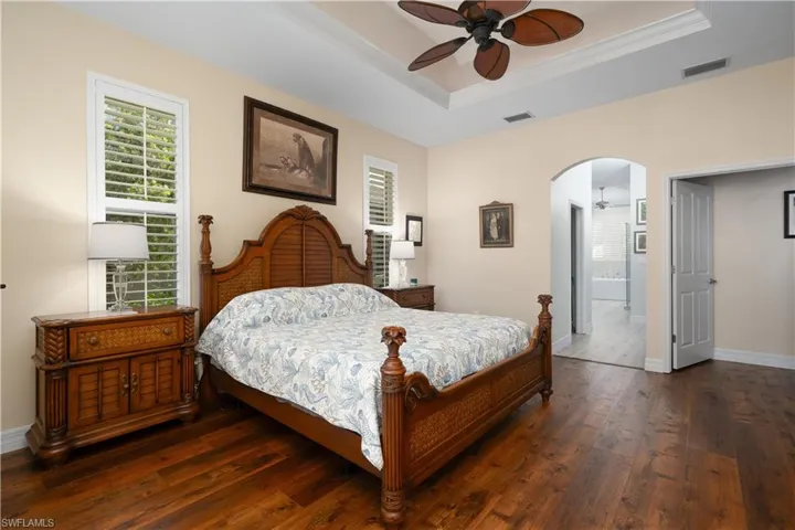 Primary bedroom with dark laminate wood flooring, arched walkways, and tray ceiling with crown molding