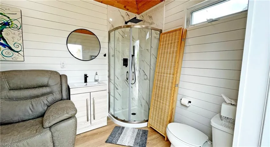 Bathroom with a stall shower, wood walls, wood finished floors, vanity, and toilet