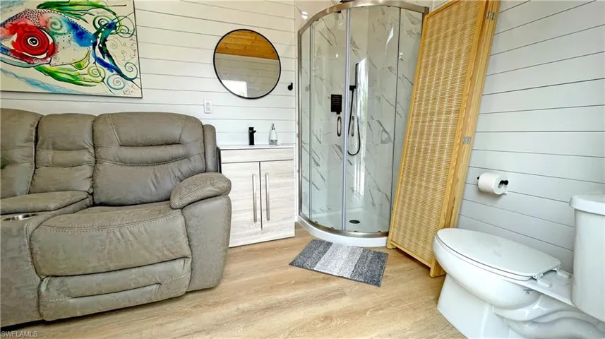 Full bath with wood walls, wood finished floors, vanity, toilet, and a marble finish shower