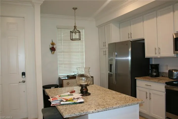Kitchen with white cabinetry, light stone countertops, appliances with stainless steel finishes, a kitchen island, and ornamental molding