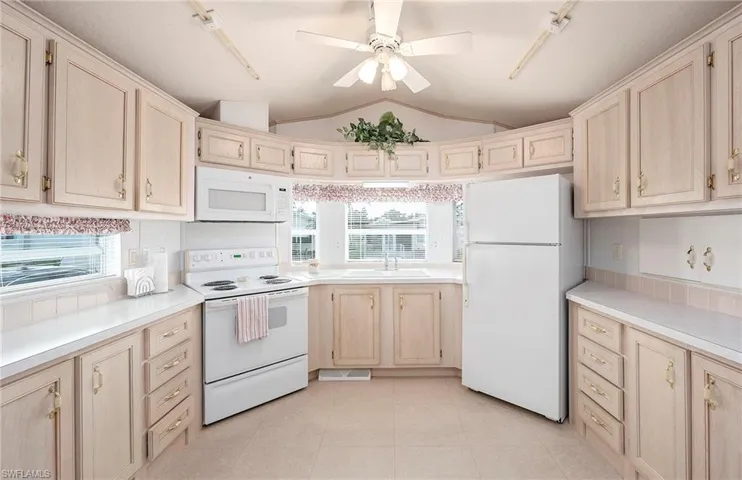 Kitchen with lofted ceiling, a healthy amount of sunlight, white appliances, and sink