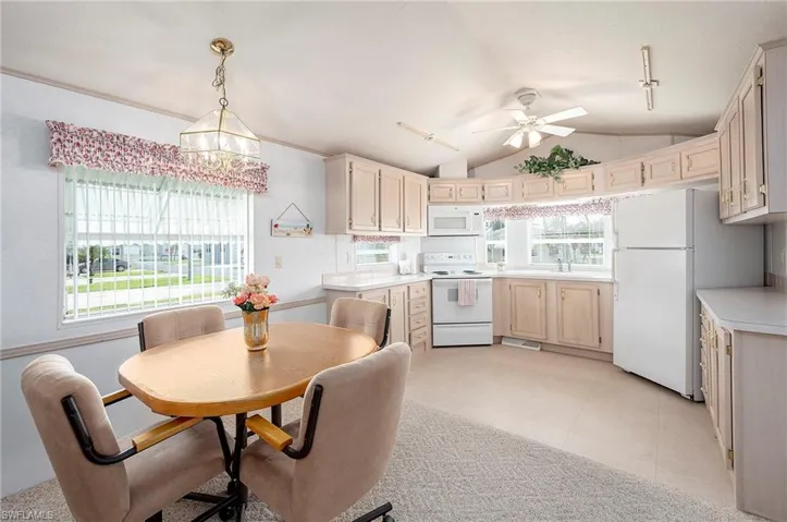 Kitchen with ceiling fan with notable chandelier, lofted ceiling, rail lighting, pendant lighting, and white appliances