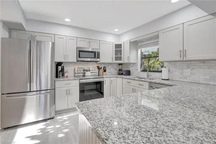 Kitchen with backsplash, light stone countertops, stainless steel appliances, and sink