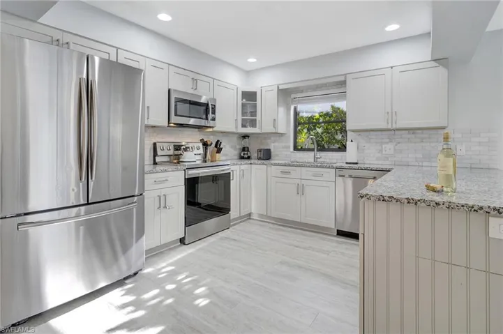 Kitchen with appliances with stainless steel finishes, white cabinetry, sink, and light stone countertops