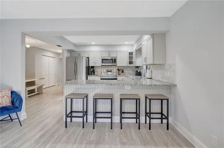 Kitchen with backsplash, light hardwood / wood-style floors, stainless steel appliances, sink, and kitchen peninsula