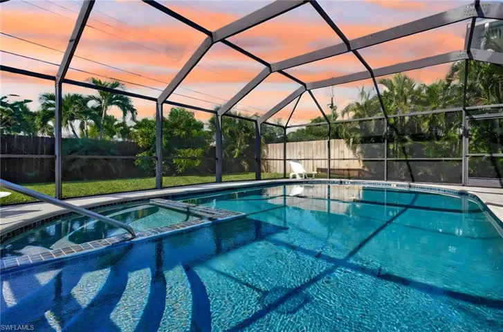 Pool at dusk featuring a lanai and an in ground hot tub