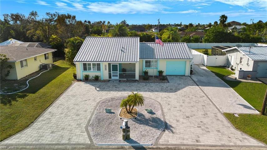 Front view of home. Tastefully landscaped exterior, metal roof, U-shaped paver driveway and extra parking area.