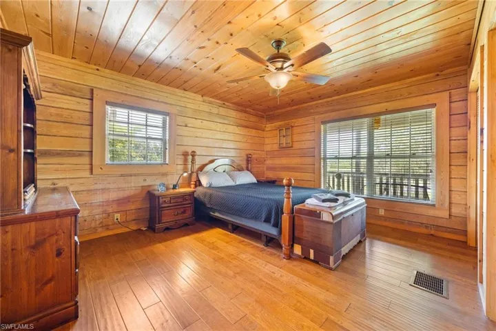 Bedroom with wooden walls, wooden ceiling, light wood-style floors, and ceiling fan