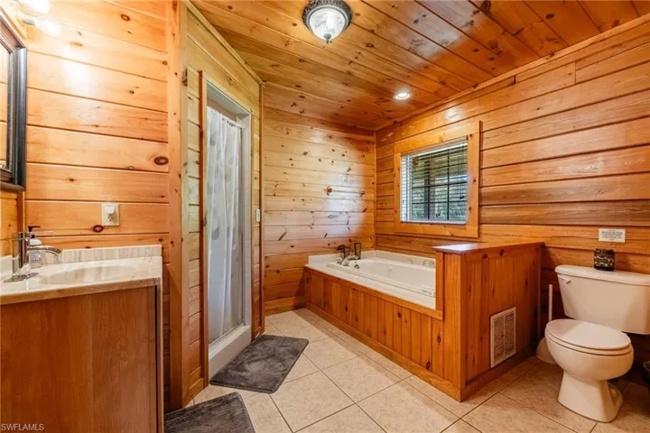 Bathroom featuring vanity, wooden walls, a shower stall, wood ceiling, and light tile patterned flooring