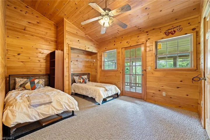 Carpeted bedroom featuring wood walls, access to outside, ceiling fan, and a vaulted wooden ceiling
