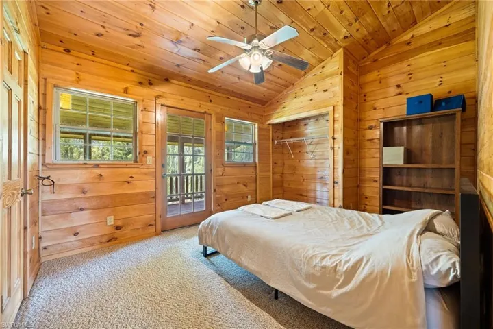 Carpeted bedroom with wooden walls, access to exterior, ceiling fan, and a vaulted wooden ceiling