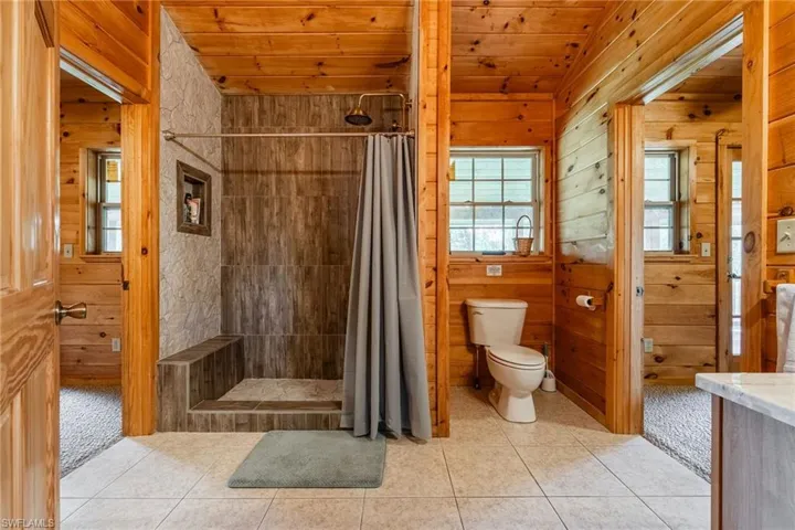 Bathroom with wooden walls, a stall shower, wood ceiling, light colored carpet, and light tile patterned floors
