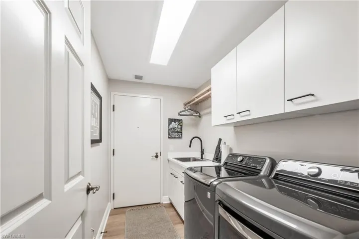 Washroom with cabinets, light wood-type flooring, sink, and washing machine and clothes dryer