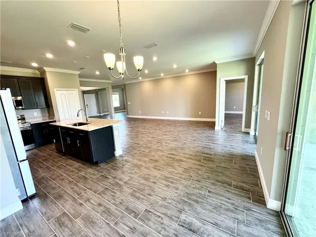 Kitchen featuring stainless steel fridge, light wood-type flooring, a center island with sink, and crown molding