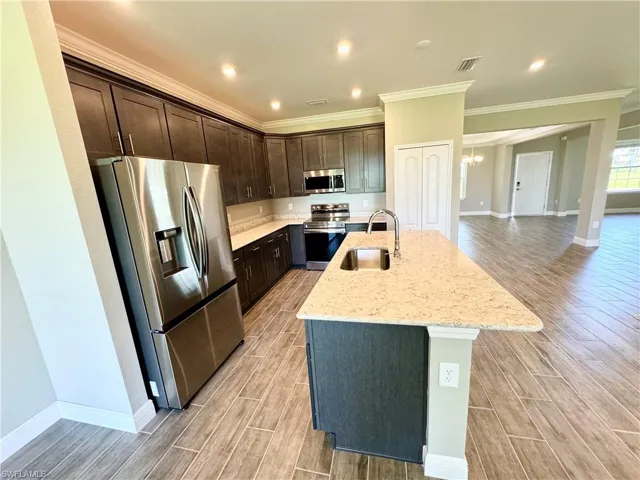 Kitchen featuring stainless steel fridge, light wood-type flooring, a center island with sink, and crown molding