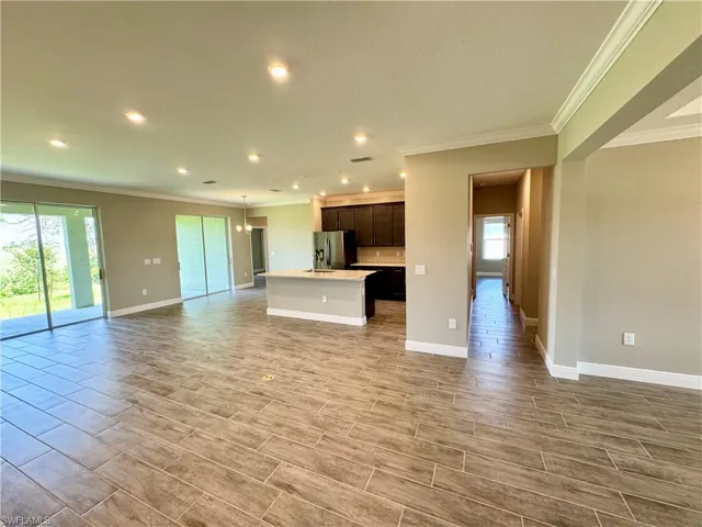 Kitchen featuring stainless steel fridge, light wood-type flooring, a center island with sink, and crown molding