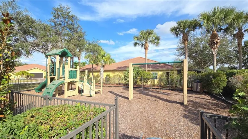 Outdoor recreational area featuring a play structure with slides, a swing set, and a perimeter fence