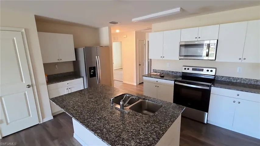 Kitchen featuring a large central island with a double basin sink, white cabinetry, speckled countertops, stainless steel appliances, and wood-finish flooring