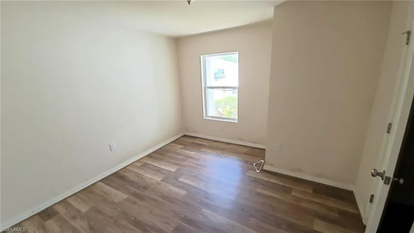 Room featuring wood-finish flooring, neutral wall paint, and a window with a white frame
