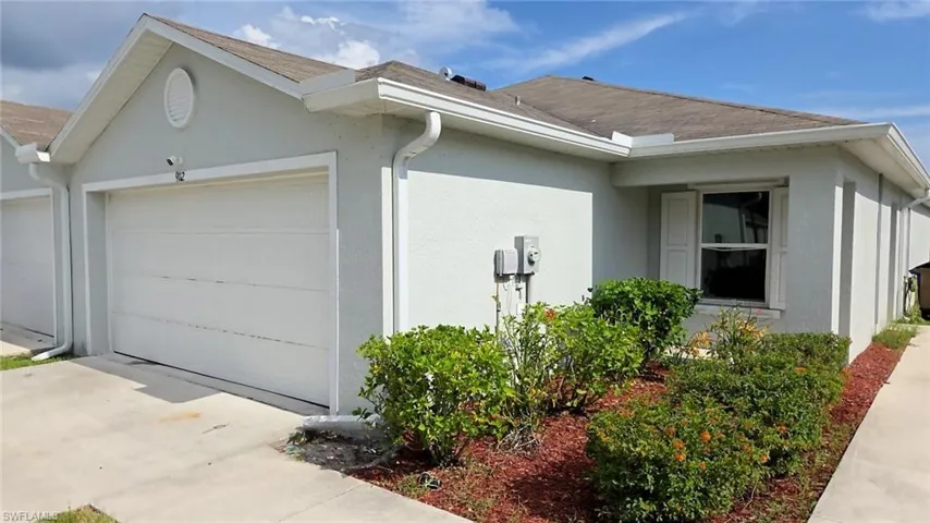 Light gray stucco exterior featuring a white garage door, white rain gutters, a shingle roof, and a front window with white louvered shutters
