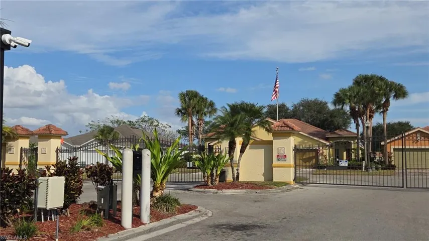 Gated community entrance featuring stucco architecture, tile roofs, and mature palm trees