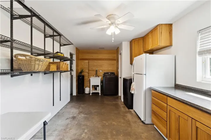 Garage pantry and laundry room with ceiling fan, white refrigerator, sink, wood walls, and washer / clothes dryer