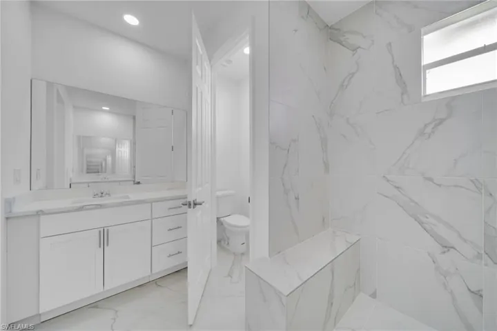 Bathroom featuring white marble-look tile, a built-in shower bench, and a modern vanity with white cabinetry