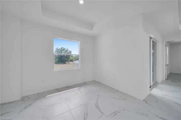 Spacious room with tray ceiling, recessed lighting, large window, and large format marble-look tile flooring