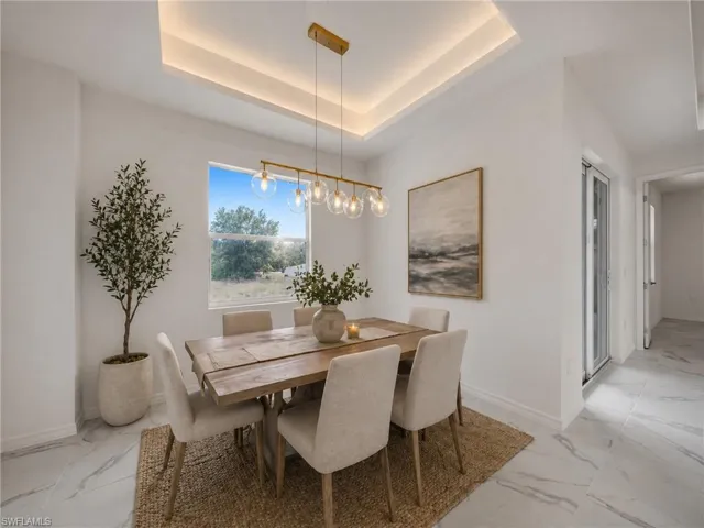 Dining area featuring a tray ceiling with accent lighting, contemporary linear chandelier, large window, and light-toned tile flooring