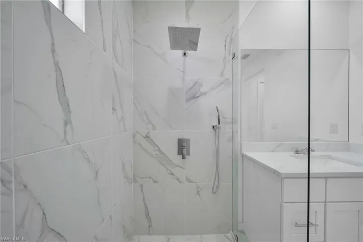 Shower enclosure featuring white marble-look tile, a rain shower head, and a hand-held spray