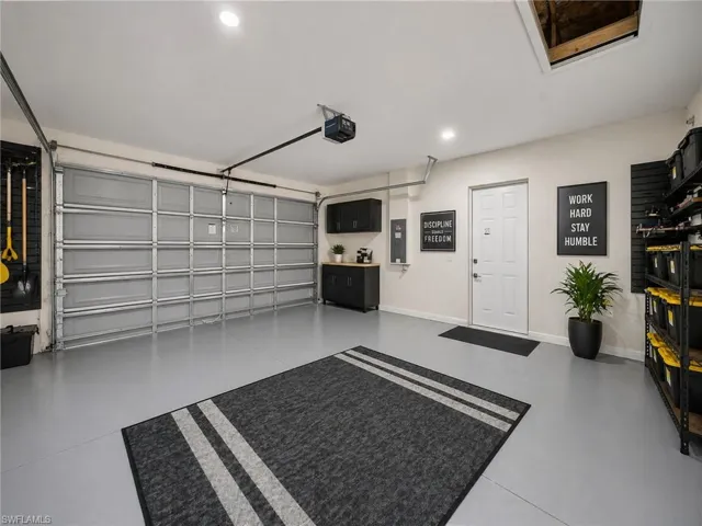 Spacious garage featuring a light gray epoxy floor coating, a white paneled door, built-in black cabinetry with a wood-finish countertop, and overhead storage shelving