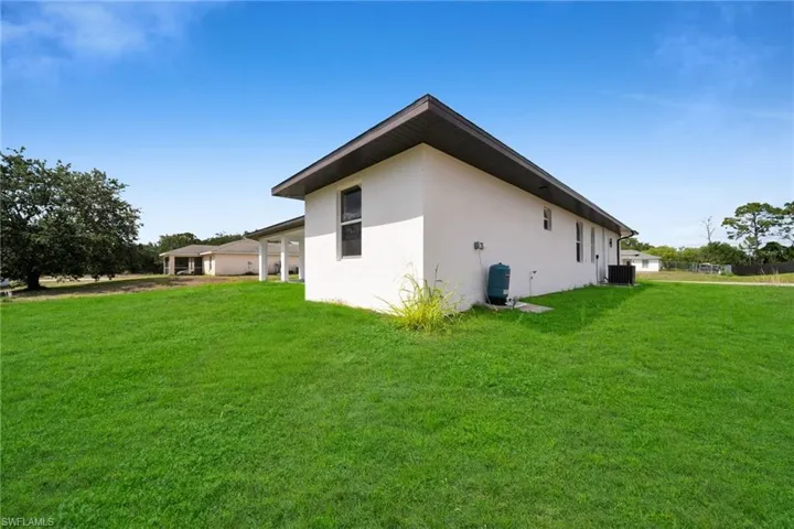 Expansive green lawn surrounds the property, featuring a white stucco exterior with multiple windows