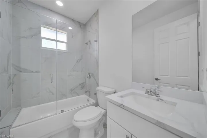 GUEST Bathroom featuring a white vanity with an integrated sink, polished chrome fixtures, a frameless mirror, and a full-size bathtub with a glass enclosure