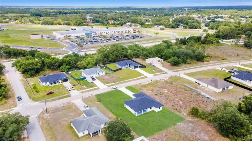 Aerial perspective of a residential neighborhood featuring several single-story homes with dark roofs and green lawns