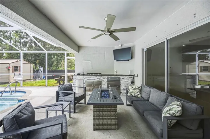 Screened patio featuring a built-in outdoor kitchen with stone veneer and stainless steel appliances, a ceiling fan, and sliding glass doors