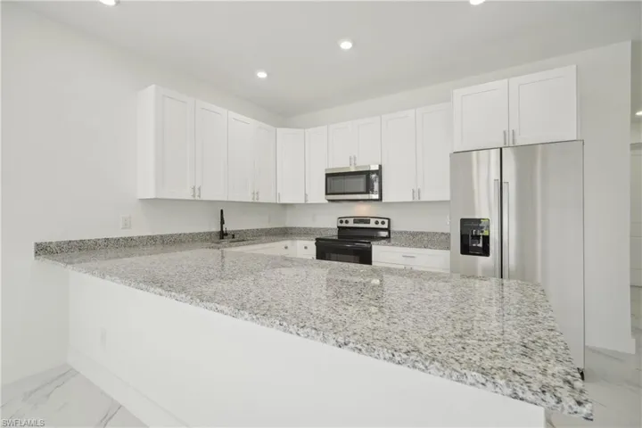 Kitchen featuring appliances with stainless steel finishes, kitchen peninsula, light stone counters, and white cabinets
