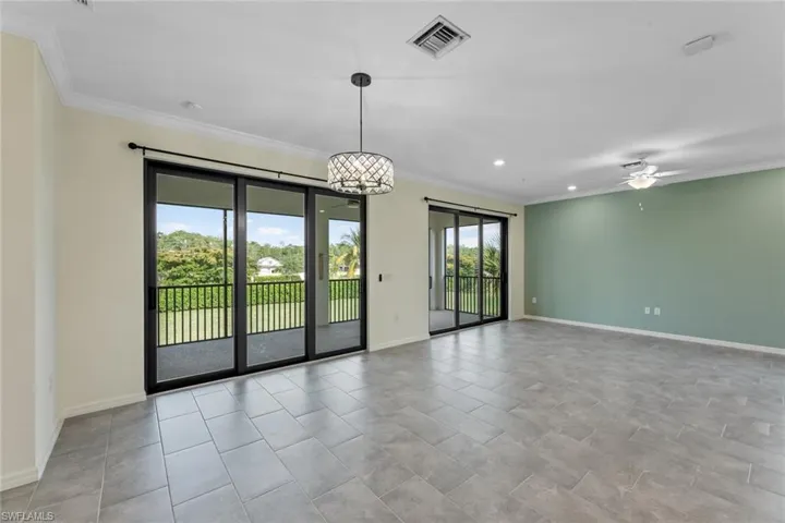 Tiled empty room featuring ceiling fan with notable chandelier and crown molding