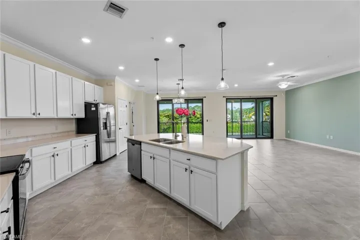 Kitchen with stainless steel appliances, white cabinets, an island with sink, and decorative light fixtures