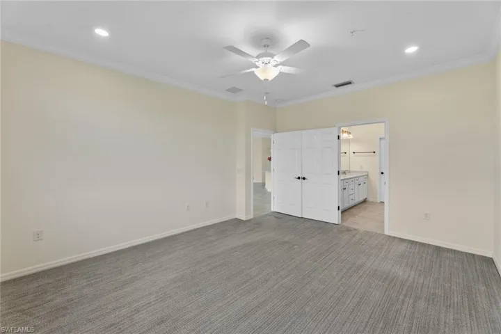 Unfurnished bedroom with ensuite bath, ceiling fan, carpet floors, and ornamental molding