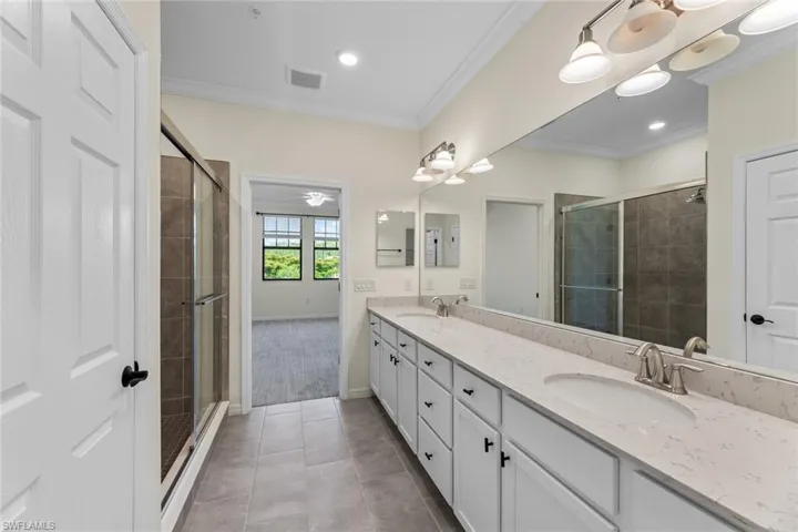 Bathroom featuring tile flooring, ornamental molding, large vanity, walk in shower, and double sink