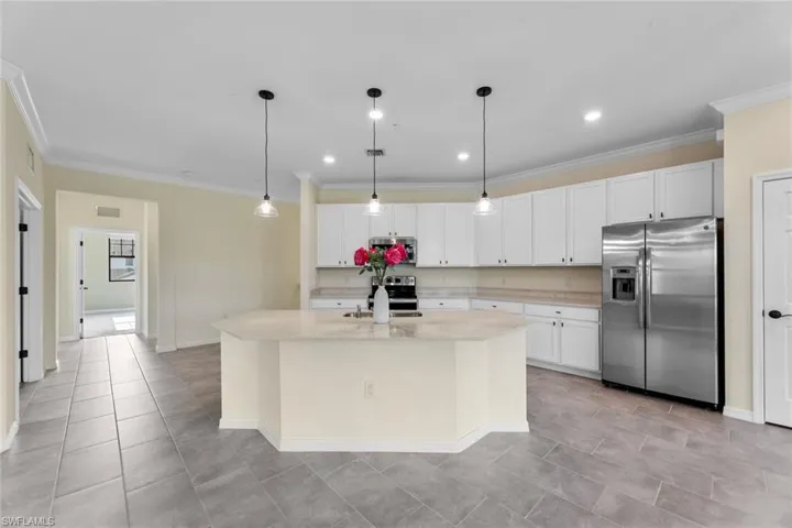 Kitchen featuring light stone counters, stainless steel appliances, hanging light fixtures, a center island with sink, and white cabinetry