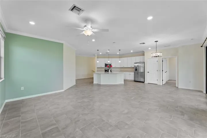 Unfurnished living room with crown molding, light tile floors, and ceiling fan with notable chandelier