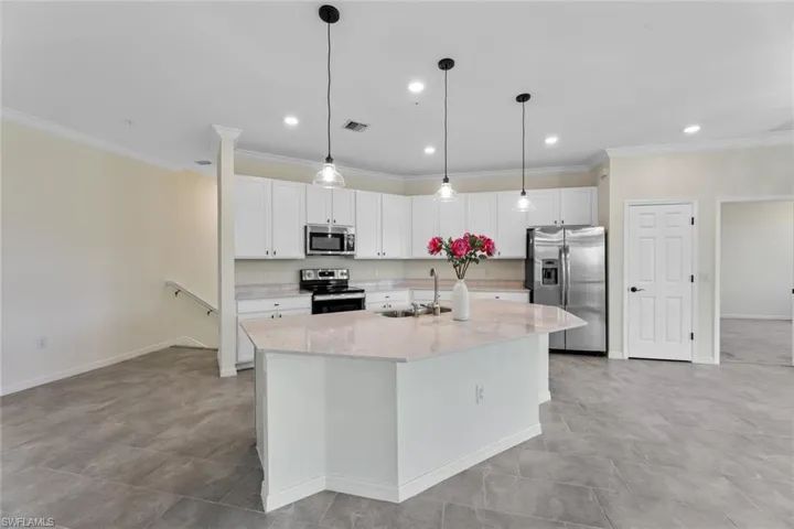 Kitchen featuring decorative light fixtures, stainless steel appliances, an island with sink, white cabinets, and sink
