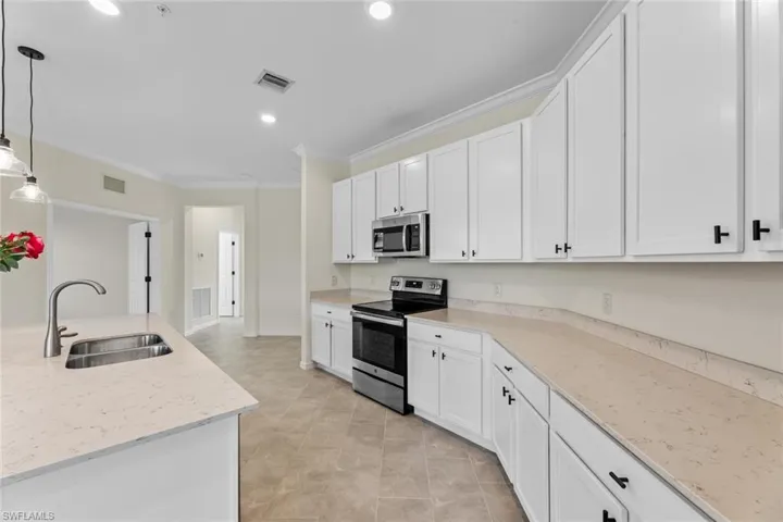 Kitchen with hanging light fixtures, stainless steel appliances, white cabinets, and sink