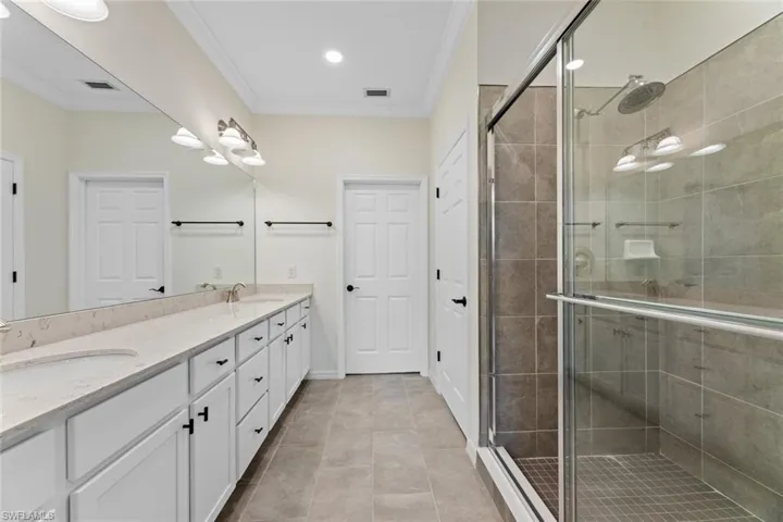 Bathroom with crown molding, tile flooring, large vanity, walk in shower, and double sink