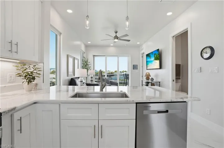 Kitchen with open floor plan, stainless steel dishwasher, light stone countertops, pendant lighting, and a peninsula - Virtually Edited Image