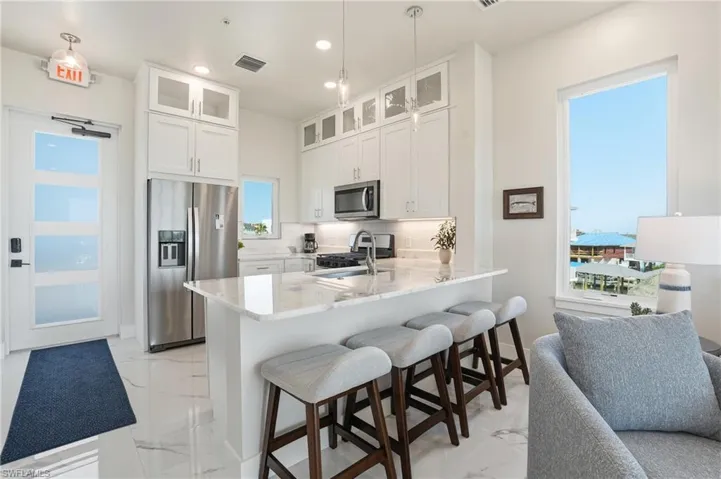 Kitchen featuring stainless steel appliances, white cabinets, a breakfast bar, light stone counters, and a peninsula - Virtually Edited Image