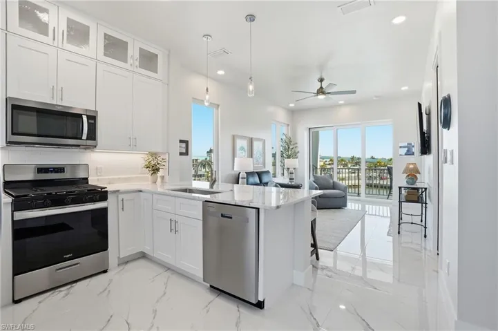 Kitchen featuring appliances with stainless steel finishes, white cabinets, light stone countertops, tasteful backsplash, and hanging light fixtures - Virtually Edited Image