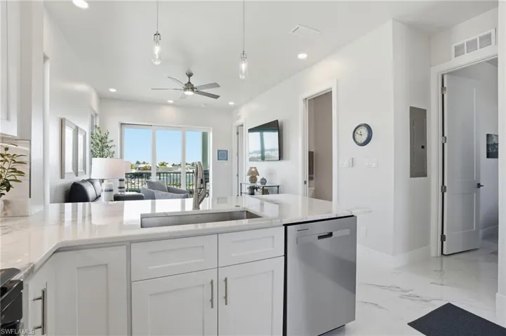 Kitchen with open floor plan, stainless steel dishwasher, white cabinetry, light stone counters, and recessed lighting - Virtually Edited Image
