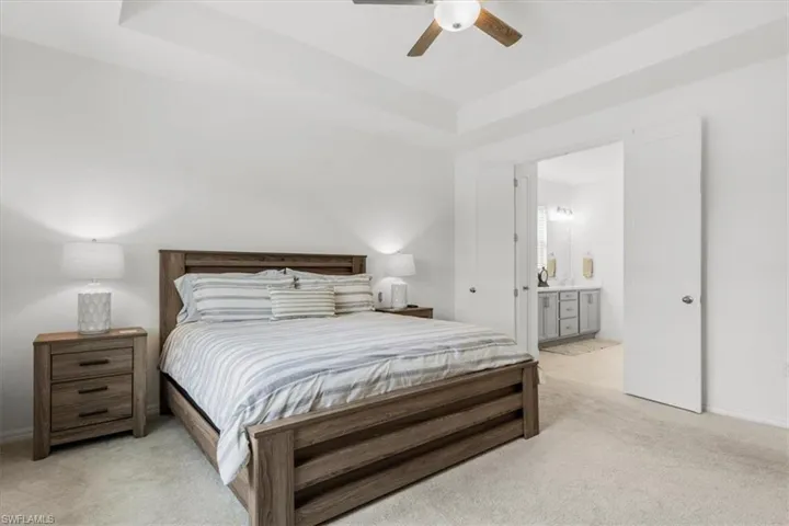 Bedroom featuring light carpet, a raised ceiling, ensuite bathroom, and ceiling fan